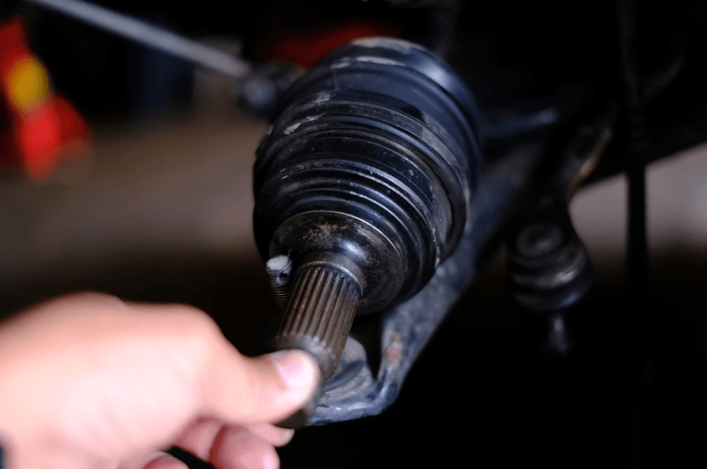 Person holding a worn CV joint with visible splined shaft and protective rubber boot in automotive repair setting