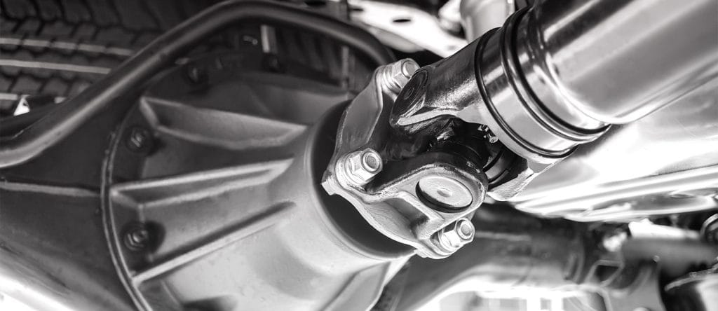 Close-up black and white view of motorcycle drive shaft connection with bolts and chrome exhaust pipe