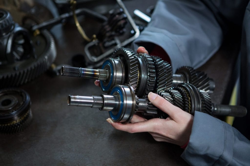 Mechanic's hands holding transmission gears and shafts in an automotive repair shop with tools in background