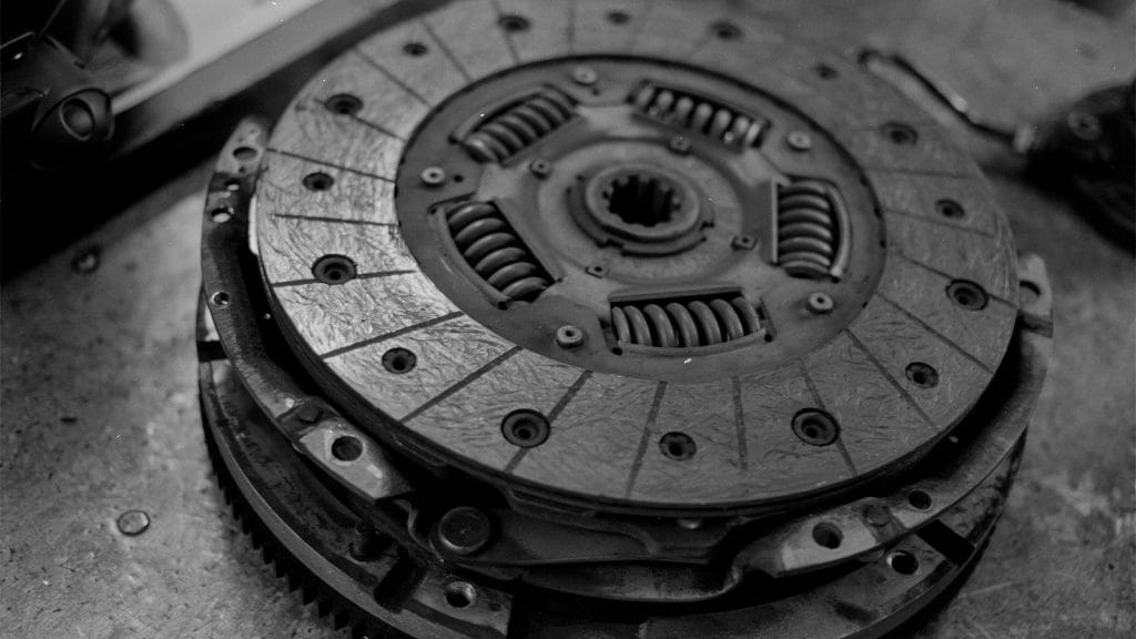 Disassembled car clutch components including clutch disc and pressure plate on workshop surface in black and white