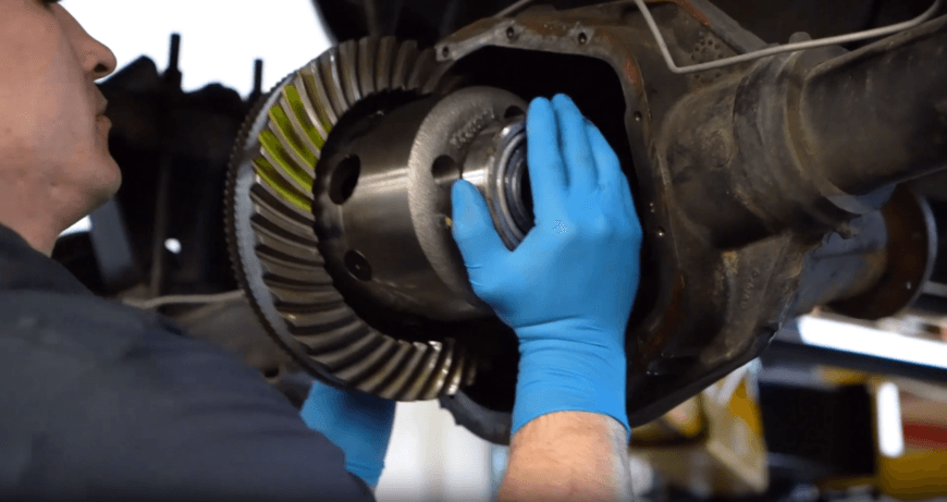 Mechanic wearing blue gloves inspecting differential gear assembly with ring and pinion gears visible